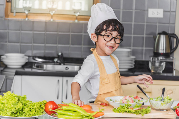Menino asiático filho cozinhar salada comida holdind colher de madeira com veget - Foto, Imagem