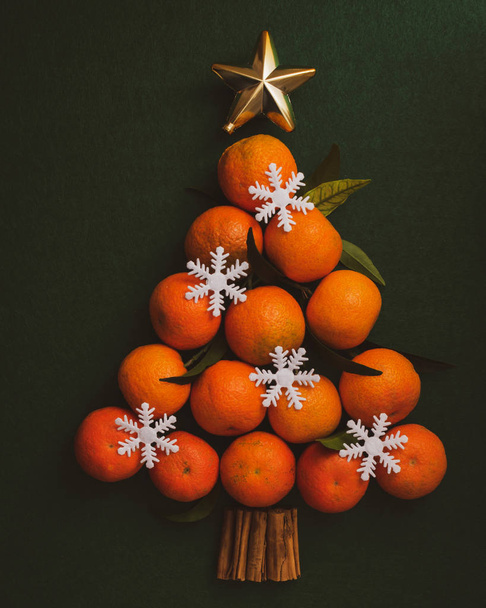 Mandarinen in Form eines Weihnachtsbaums auf dunkelgrünem Hintergrund. - Foto, Bild