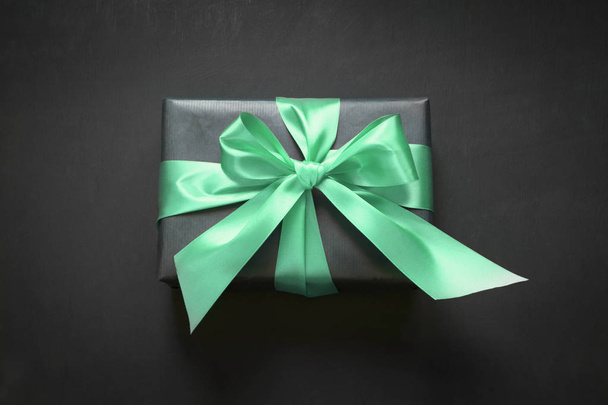 Gift box wrapped in black paper with neo mint ribbon on black surface. - 写真・画像