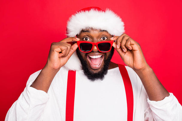 Close up photo of astonished african santa claus touching his specs screaming wow omg see noel miracle wearing stylish white sweater isolated over red background - Foto, immagini