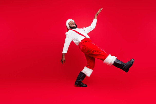Full size profile side photo of cheerful black santa claus going moving laughing wearing white pullover pants trousers isolated over red background - Foto, Bild
