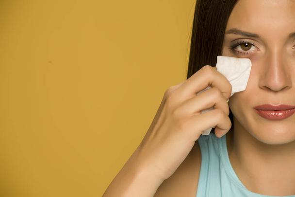junge Frau reinigt ihr Gesicht mit Feuchttüchern auf gelbem Hintergrund - Foto, Bild
