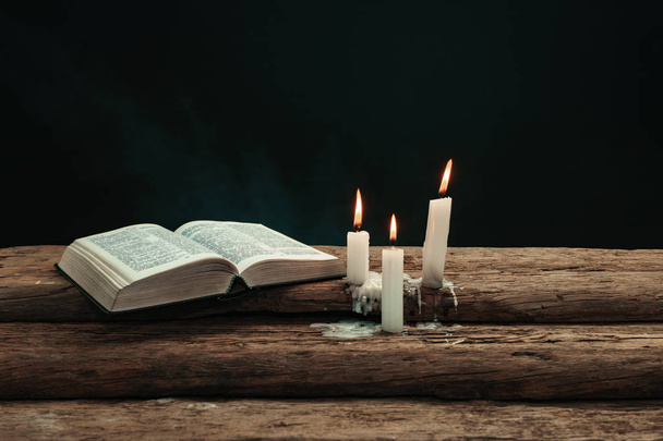 Gyönyörű nyitott Bibliát, és égett gyertyát egy régi tölgyfából készült asztal. Háttere füst. - Fotó, kép