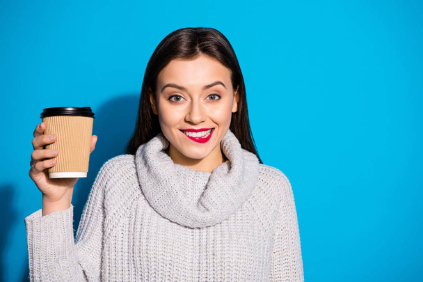 Portrait of cute funky lady holding hot americano espresso biting her lip wearing gray jumper isolated over blue background - Фото, изображение