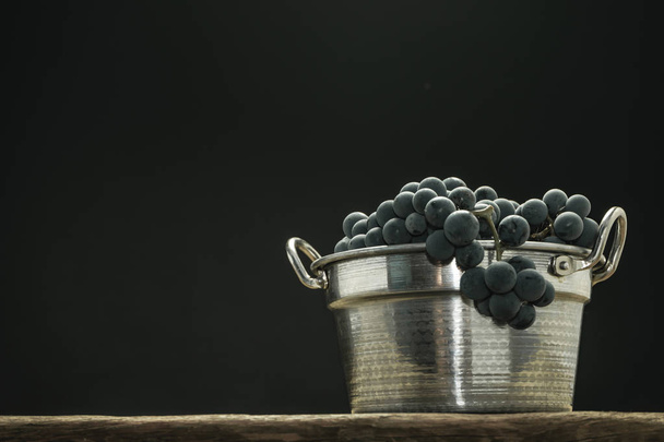 Beautiful wine grapes of silver basket on a old oak wooden table and black background. - Photo, Image