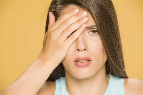 Jeune femme avec douleur dans les yeux et la tête sur fond jaune
 - Photo, image