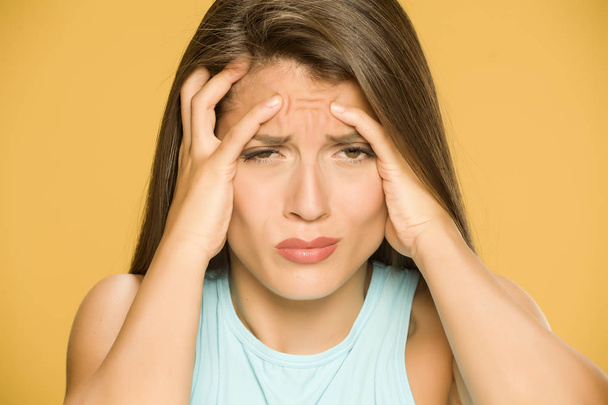 Mujer joven con fuerte dolor de cabeza sobre fondo amarillo
 - Foto, Imagen
