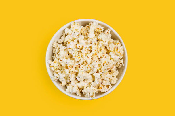 Popcorn in a white bowl on a yellow background - Фото, зображення