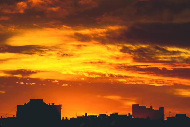 Cityscape with vivid fiery dawn. Amazing warm dramatic cloudy sky above dark silhouettes of city buildings. Orange sunlight. Atmospheric background of sunrise in overcast weather. Copy space. - Photo, Image