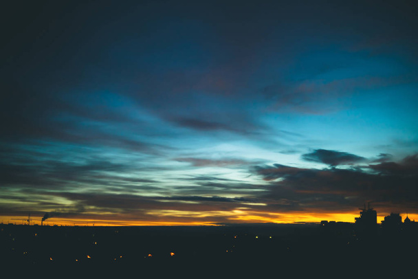 Міський пейзаж з чудовим різнокольоровим яскравим світанком. Дивовижне блакитне хмарне небо над темними силуетами міських будівель. Атмосферний фон оранжевого сходу сонця в похмуру погоду. Копіювати простір
. - Фото, зображення