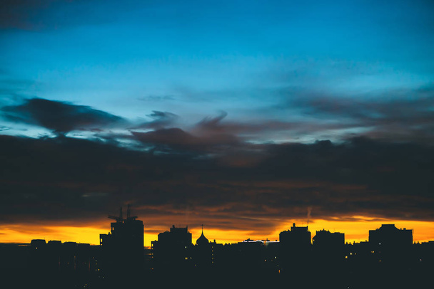 Αστικό τοπίο με υπέροχη ποικιλία έντονη αυγή. Εκπληκτική δραματική γαλάζια συννεφιά πάνω από τις σκοτεινές σιλουέτες των κτιρίων της πόλης. Ατμοσφαιρικό φόντο πορτοκαλί Ανατολή σε συννεφιασμένη καιρό. Αντιγραφή χώρου. - Φωτογραφία, εικόνα