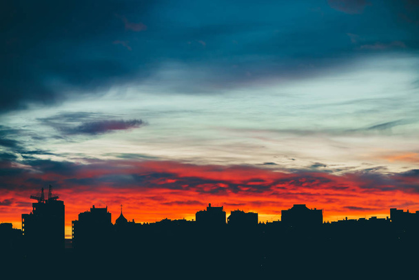Cityscape with wonderful varicolored vivid dawn. Amazing dramatic multicolored cloudy sky above dark silhouettes of city buildings. Atmospheric background of sunrise in overcast weather. Copy space. - 写真・画像