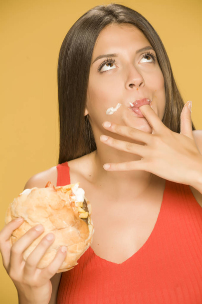 Молода жадібна жінка їсть бургер на жовтому фоні
 - Фото, зображення