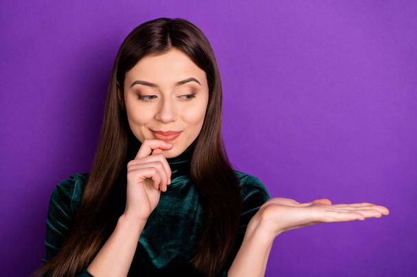 Portrait of interested lady looking at her palm touching chin wearing black velvet turtleneck isolated over purple violet background - Photo, Image