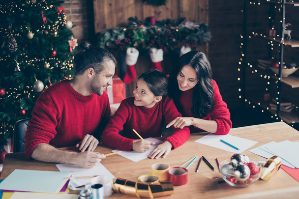 Photo of nice smiling cheerful kind family schoolgirl wearing red jumpers writing letters to santa claus in friendly atmosphere in eve of new year - 写真・画像