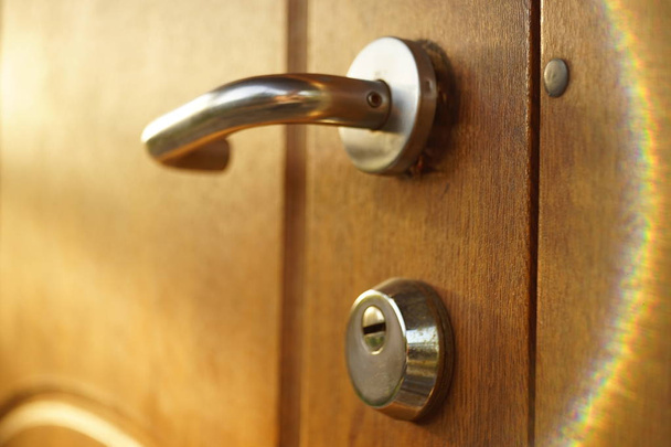 bruine houten deur met chroom handvat en sleutelgat, mooie zonnestralen - Foto, afbeelding