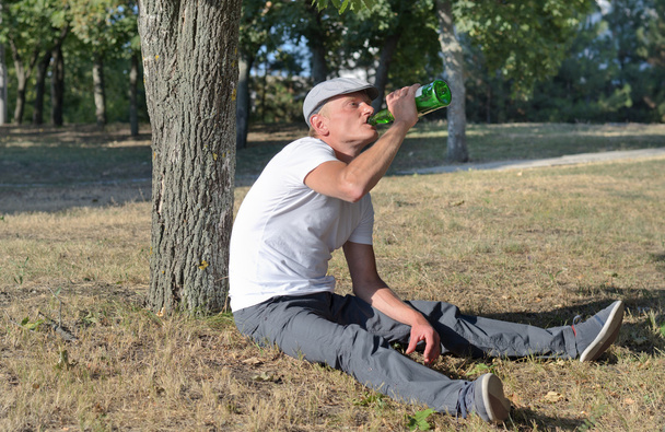 Alcoólico sentado bebendo em um parque
 - Foto, Imagem