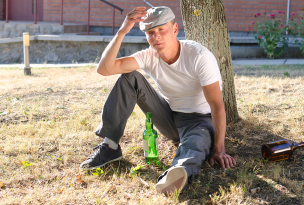 Betrunkener sitzt am Fuß eines Baumes - Foto, Bild