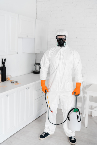 Exterminator w maskę ochronną i jednolite gospodarstwa toksyczne urządzenia stojąc w pobliżu szafki kuchennej  - Zdjęcie, obraz