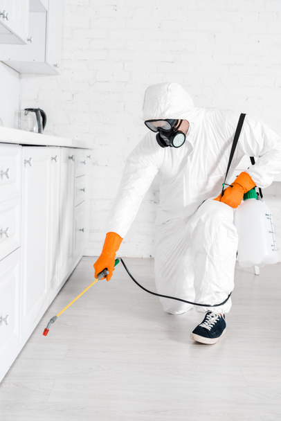 exterminador em máscara protetora usando spray tóxico perto do armário da cozinha
  - Foto, Imagem