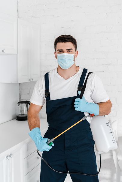 exterminator in protective mask and uniform holding toxic spray and looking at camera - Photo, Image