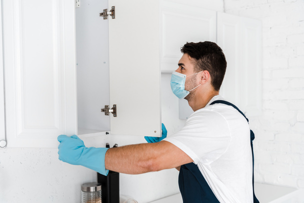 exterminator in uniform looking at kitchen cabinet  - Photo, Image