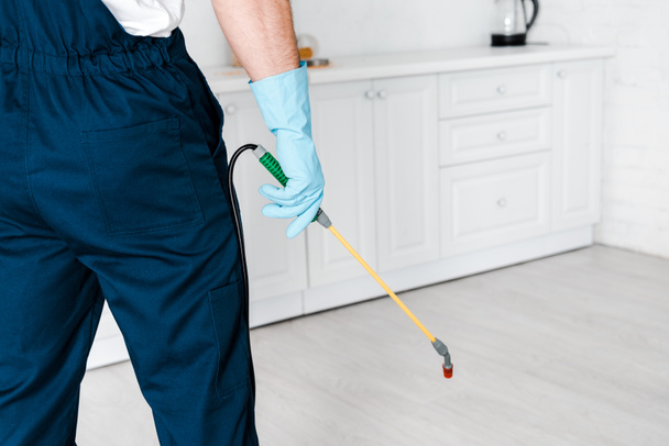 cropped view of exterminator in uniform holding spray with pesticide near kitchen cabinet  - 写真・画像