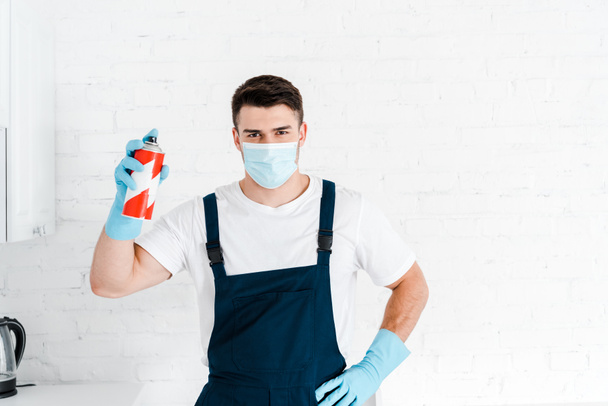 Εξολοθρευτής σε γάντια λατέξ κρατώντας τοξικό σπρέι μπορεί και στέκεται με το χέρι στο ισχίο  - Φωτογραφία, εικόνα