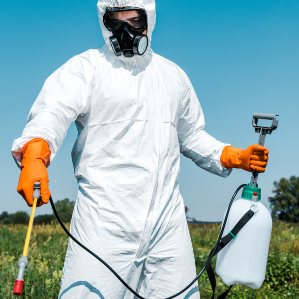 exterminator in orange latex gloves and white uniform holding spray outside  - Foto, Imagen
