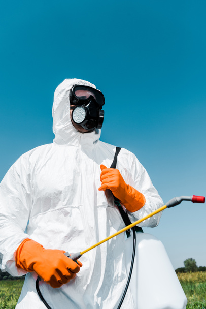 exterminator in orange latex gloves holding toxic spray against sky  - Фото, изображение