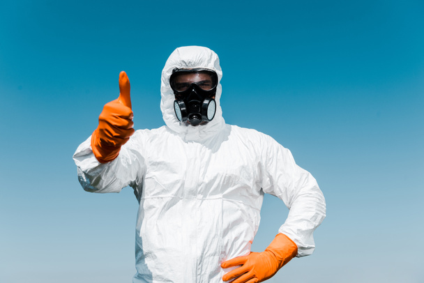 exterminator in protective mask and uniform standing with hand on hip and showing thumb up  - Photo, Image