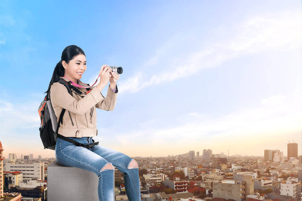 Asian woman with a backpack sitting on the rooftop and holding a - Foto, Imagen