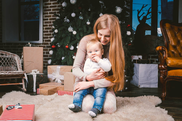 mladá matka a syn hrají blízko vánočního stromku. mladá matka a syn hráli blízko vánočního stromku. Vánoční Slavnostní večer. Máma a syn na podlaze pod vánočním stromku - Fotografie, Obrázek
