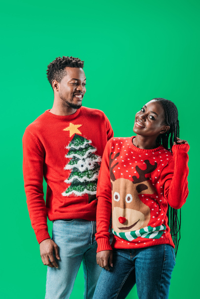 African American man and woman in Christmas sweaters isolated on green - 写真・画像
