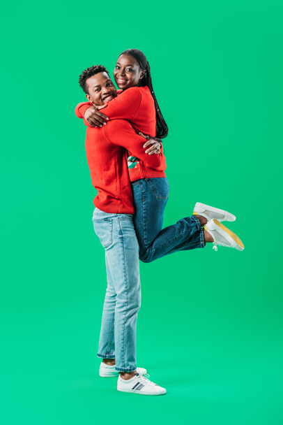 African American mężczyzna trzyma kobietę w czerwonym swetrze bożonarodzeniowy na zielono - Zdjęcie, obraz
