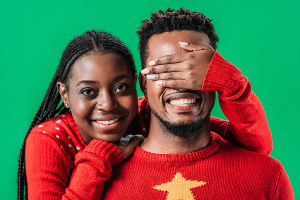 African American woman in red sweater covering eyes with hand to man isolated on green - Foto, Imagem