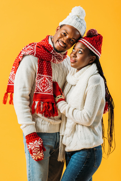 African American man in winter outfit embracing woman who looking at him isolated on yellow - Fotó, kép