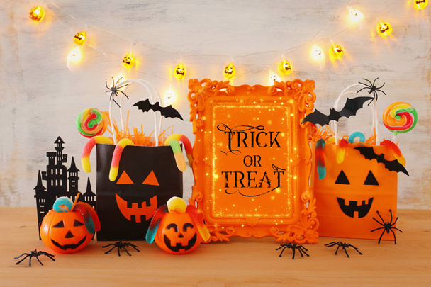 holidays image of Halloween. Pumpkins, bats, treats, paper gift bag over wooden table - Photo, Image