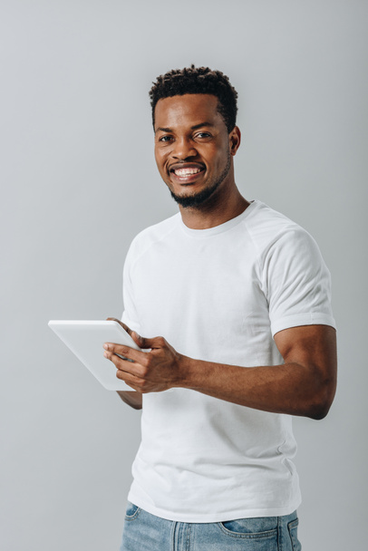 Gelukkig Afro-Amerikaanse man met digitale Tablet en kijken naar camera geïsoleerd op grijs - Foto, afbeelding