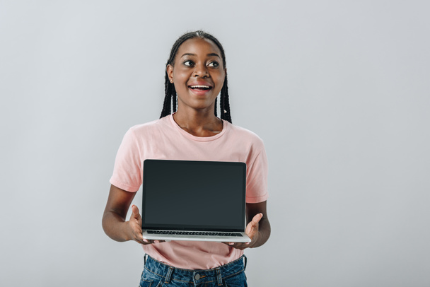 excited African American woman holding laptop with blank screen and looking away isolated on grey - Photo, Image