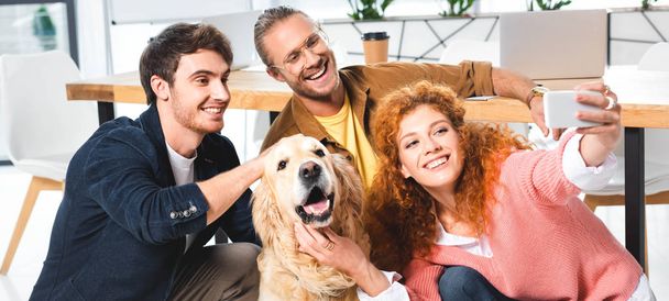 panoramic shot of three smiling friends taking selfie with cute golden retriever - Foto, imagen