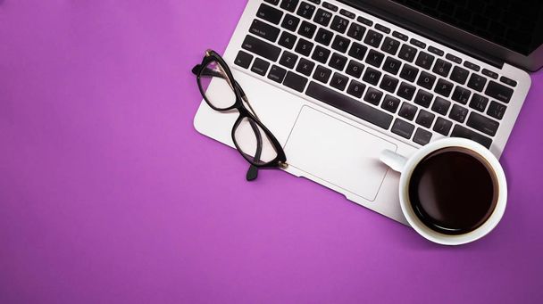 gray laptop with  cup of coffee and glasses on purple background table, working place at home or in the office - Photo, image