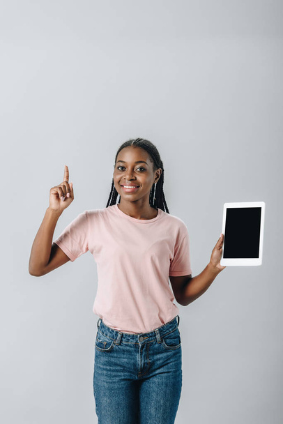 African American woman holding digital tablet with blank screen and showing idea sign isolated on grey - Photo, image