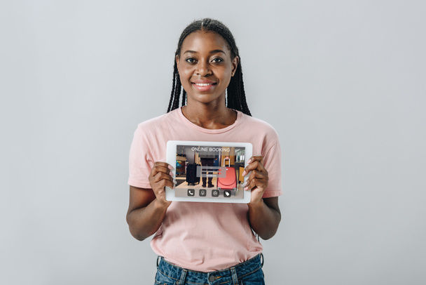 灰色で隔離されたオンライン予約アプリケーションでカメラデジタルタブレットで示すアフリカ系アメリカ人の女性 - 写真・画像