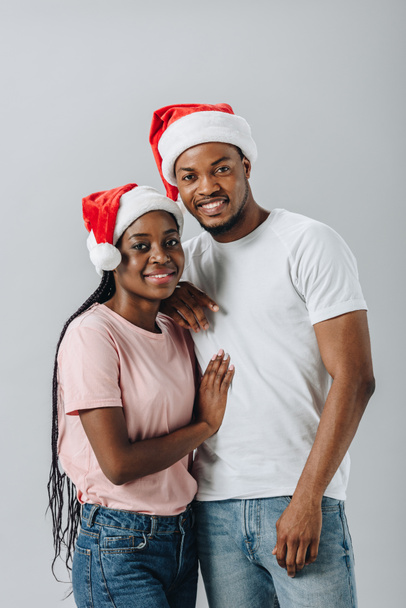 Афроамериканская пара в шляпах Санта-Клауса смотрит на камеру, изолированную от серых
 - Фото, изображение