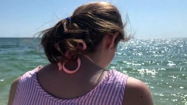 Close-up zijaanzicht van een jonge blanke vrouw die op een strand staat met zijn armen in de lucht, met uitzicht op zee - Video
