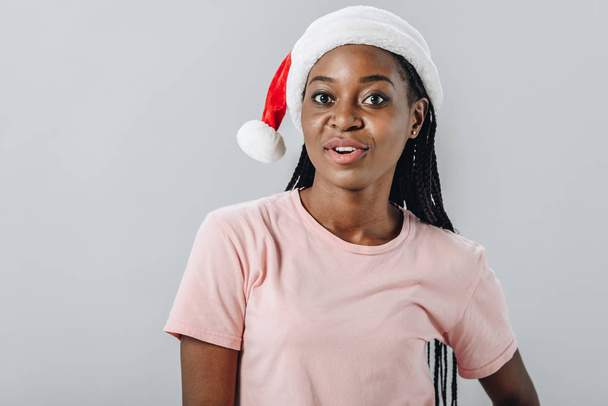Santa şapka lı Afro-Amerikalı kadın ve t-kısa gri izole kamera bakıyor - Fotoğraf, Görsel