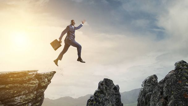 Black businessman jumping over mountain stones - Zdjęcie, obraz