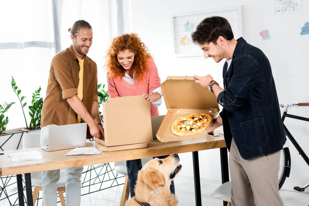 three smiling fiends holding boxes with pizza in office  - Photo, Image