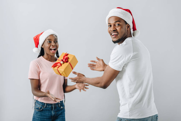 Афроамериканець пара в Санта-капелюх кидати Подарункова коробка ізольований на сірий - Фото, зображення